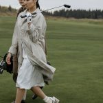 A fashionable couple walking with golf equipment on a lush green course.