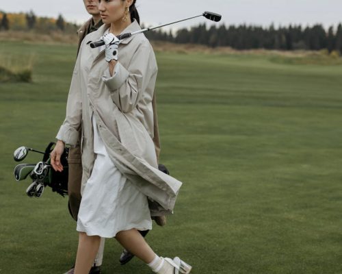 A fashionable couple walking with golf equipment on a lush green course.